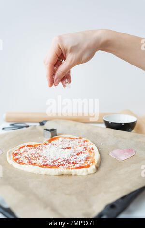 Pasta per pizza a forma di cuore, lo chef cosparge la pizza con parmigiano. Il concetto di una sorpresa per St. San Valentino Foto Stock