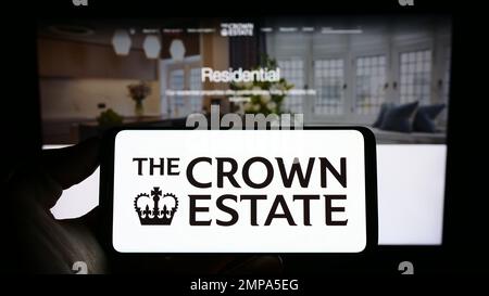 Persona che tiene il cellulare con il logo della società britannica Crown Estate statutaria sullo schermo di fronte al sito web aziendale. Messa a fuoco sul display del telefono. Foto Stock