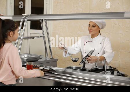 Operaio della mensa della scuola alla linea di servizio. Cibo gustoso Foto Stock