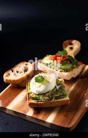 Toast all'uovo in camicia e all'avocado su tavola di legno su fondo in ardesia nera Foto Stock