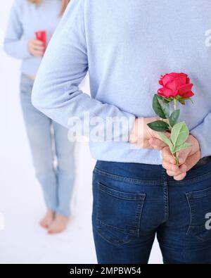 Giovane uomo attraente che tiene una rosa dietro la schiena per sorprendere il suo amante. Foto Stock