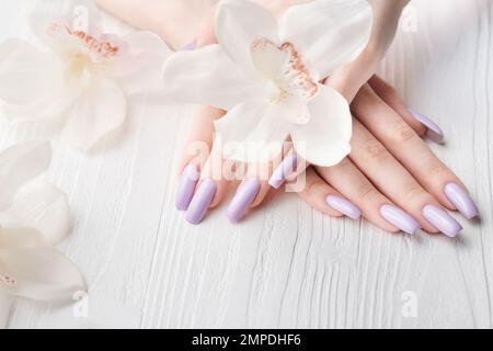 Mani di ragazza con delicata manicure viola e fiori di orchidea. Il concetto di bellezza e cura del corpo. Foto Stock