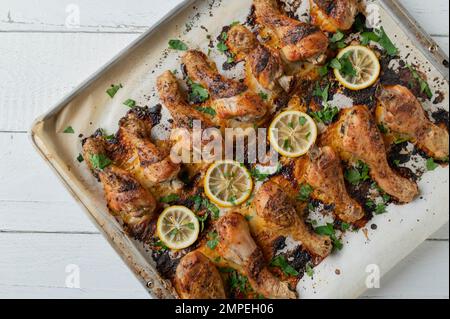 Fiammiferi di pollo arrostiti al forno su una teglia da forno con erbe e limone isolati su fondo bianco. Giacitura piatta Foto Stock