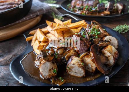 Bratwurst con cipolla bruna, salsa di funghi e patatine fritte fatte in casa su tavola di legno. Foto Stock