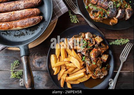 Pasto bratwurst con cipolla, salsa di funghi e patatine fritte su tavola di legno. Giacitura piatta Foto Stock