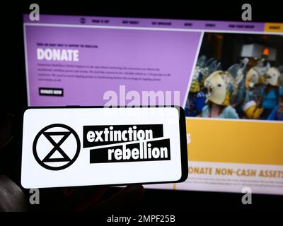 Persona che tiene il cellulare con il logo dell'organizzazione Extinction Rebellion (XR) sullo schermo di fronte alla pagina web. Messa a fuoco sul display del telefono. Foto Stock