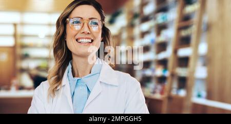Operatore sanitario in piedi in farmacia in un camice bianco. Donna che lavora in una farmacia. Donna farmacista sorridente. Foto Stock