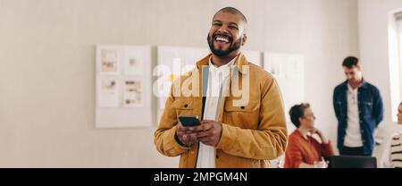 Allegro uomo d'affari con un anello a setto che sorride alla fotocamera mentre tiene uno smartphone. Felice giovane uomo d'affari che lavora in un wor creativo e moderno Foto Stock