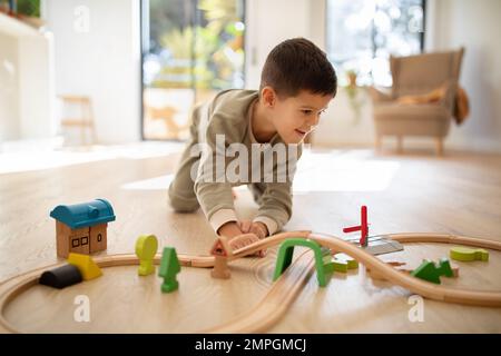 Felice ragazzo allegro piccolo europeo in pigiama sul pavimento gioca con la strada e le auto da solo, godere di fantasia a tempo libero Foto Stock