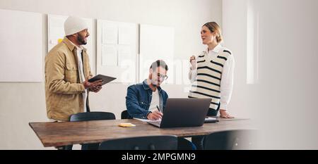 Felici colleghi sorridenti mentre lavorano insieme in un ufficio creativo. Gruppo di diverse aziende che lavorano con la tecnologia wireless in un minuto Foto Stock