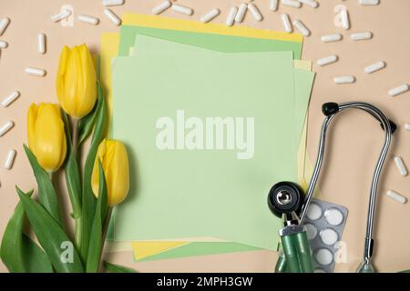 Primavera e medicina - tulipani gialli e stetoscopio con spazio per il testo su sfondo verde chiaro. Foto Stock