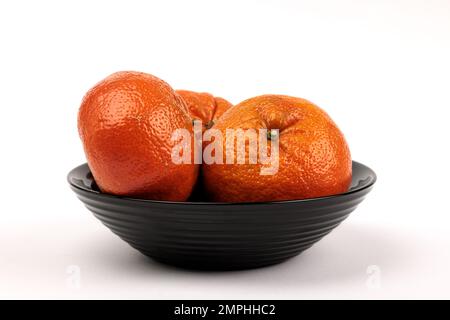 Tre tangerini in una terrina di frutta nera su fondo bianco. Foto Stock