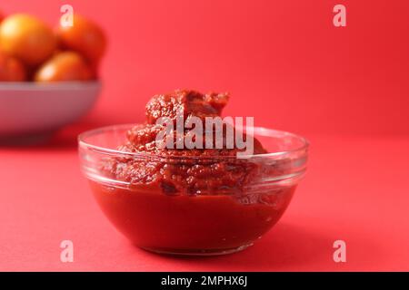 concentrato di pomodoro in una ciotola di salsa di vetro su un monocolor di fondo rosso. Cibo salsa di pomodoro rosso cibo. Foto Stock