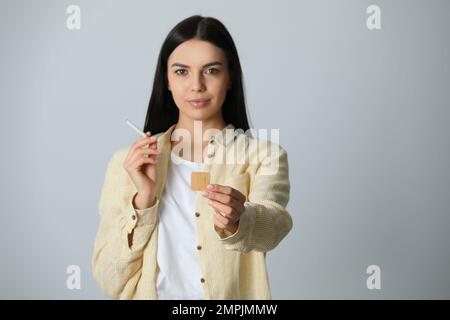 Giovane donna felice con nicotina cerotto e sigaretta su sfondo grigio chiaro Foto Stock