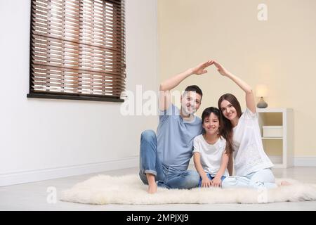 Famiglia felice che forma il tetto della casa con le loro mani a casa. Concetto di assicurazione Foto Stock