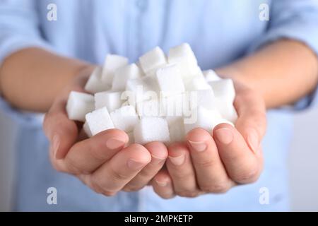 Donna che tiene un mucchio di cubetti di zucchero raffinati, primo piano Foto Stock