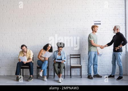 produttore bearded che scuote le mani con l'uomo rosso vicino agli attori interrazziali. Traduzione del tatuaggio: kanji, pericolo Foto Stock