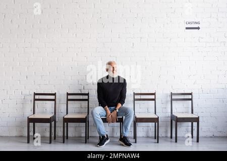 uomo barbuto sorridente ad occhi chiusi mentre si siede sulla sedia e in attesa di casting Foto Stock