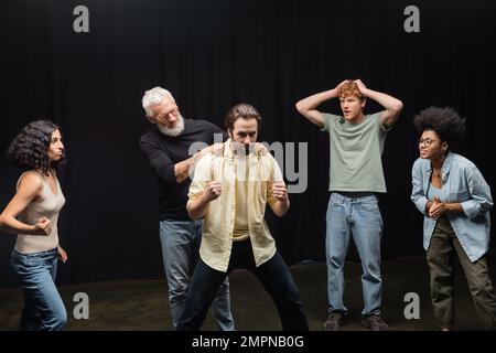 insegnante di capacità recitative beared che tocca le spalle del giovane uomo durante le prove presso attori multietnici. Traduzione del tatuaggio: om, shanti, pace Foto Stock