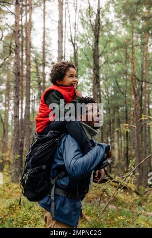 Vista laterale del padre che trasporta il figlio sulla spalla mentre esplora la foresta durante la vacanza Foto Stock