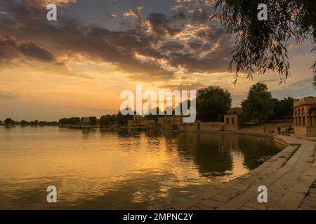 Spettacolare tramonto sul lago Gadisar, Jaisalmer, Rajasthan, India. Sole e nuvole colorate nel cielo con vista sul lago Gadisar. Connessione WIT Foto Stock