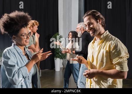 vista laterale di sorridenti studenti multietnici e insegnante di capacità di recitazione parlando e gesturing nella scuola di teatro Foto Stock