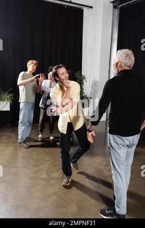 uomo eccitato che prova il produttore vicino di mezza età e gli attori interrazziali che parlano sullo sfondo sfocato Foto Stock
