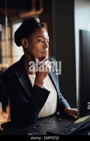 Donna d'affari premurosa con mano sul mento che lavora in ufficio Foto Stock