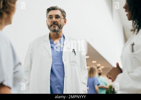 Un medico di sesso maschile maturo che indossa un camice da laboratorio che discute con i colleghi in ospedale Foto Stock