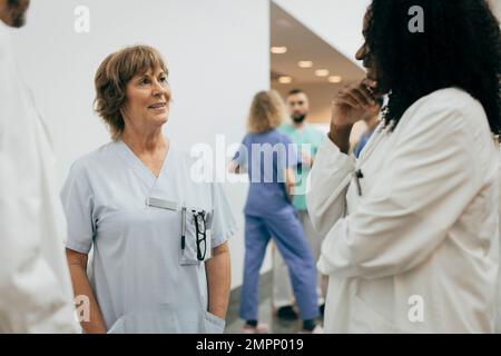 Sorridente medico femminile con le mani in tasca a discutere con un collega in ospedale Foto Stock