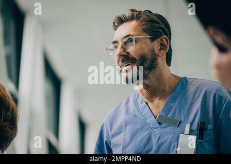 Vista dal basso angolo di un medico maschile sorridente e maturo che indossa occhiali in ospedale Foto Stock