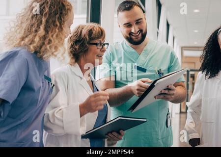 Sorridente squadra medica multirazziale che discute sopra la clipboard in ospedale Foto Stock