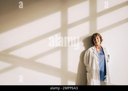 Ritratto di medico maturo in piedi contro il muro con ombra Foto Stock