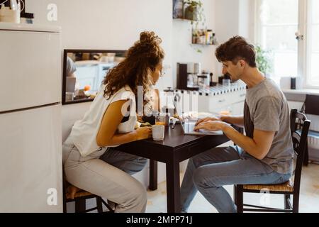 Uomo che parla con una donna mentre usa un computer portatile sul tavolo da pranzo a casa Foto Stock