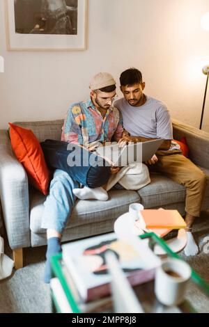 Coppia gay che usa il computer portatile mentre si siede sul divano a casa Foto Stock