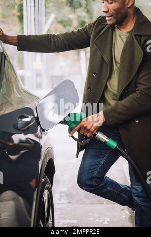 Uomo maturo che pompa gas in auto mentre si trova in piedi presso la stazione di rifornimento Foto Stock