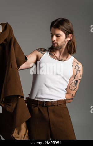 Uomo dai capelli lunghi con giacca da tatuaggio isolata sul grigio Foto Stock