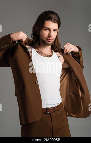 Uomo trendy a capelli lunghi con giacca da tatuaggio isolata sul grigio Foto Stock