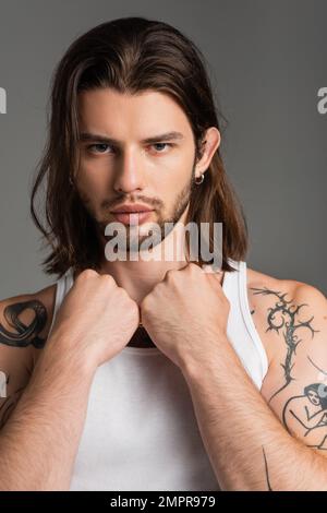 Ritratto di un uomo tatuato e a capelli lunghi che guarda la telecamera isolata sul grigio Foto Stock