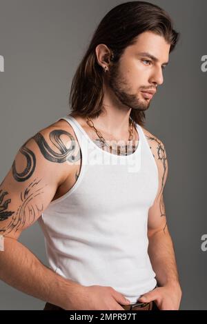 Uomo dai capelli lunghi con tatuaggio sul corpo che posa isolato sul grigio Foto Stock
