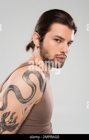 Ritratto di modello tatuato a capelli lunghi guardando la telecamera isolata sul grigio Foto Stock