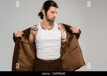 Uomo dai capelli lunghi tatuato che indossa una giacca isolata sul grigio Foto Stock