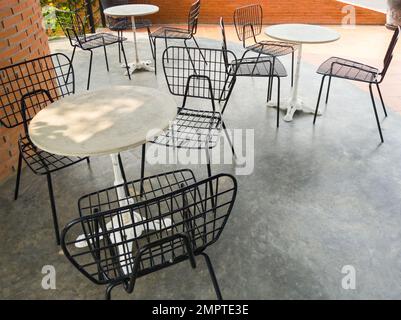 La moderna sedia in metallo con il piccolo tavolo bianco vicino alla parete in mattoni della caffetteria, vista frontale con lo spazio copia. Foto Stock