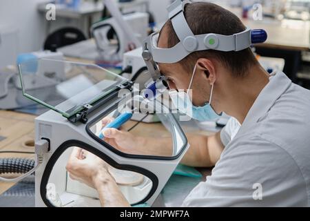 Dentista mulini a mano corone di denti creato su 3D stampante per metallo. Tecnico odontoiatrico che lavora con corone in ceramica in scatola protettiva presso il laboratorio. Foto Stock