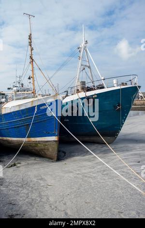 Due barche da pesca scafi blu sulla sabbia con bassa marea nel porto dell'isola a ovest dell'Irlanda in una soleggiata giornata autunnale a Kilronan Aran Islands County Galway. Foto Stock