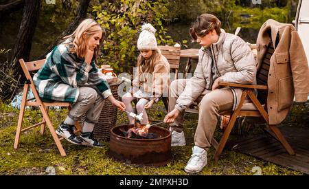 Bambini, famiglia, sorella fratello friggere marshmallows sul fuoco. Picnic nella natura. Sedia di legno, table.barbecue barbecue cibo. Viaggio di vacanza, fine settimana di vacanza dinne Foto Stock