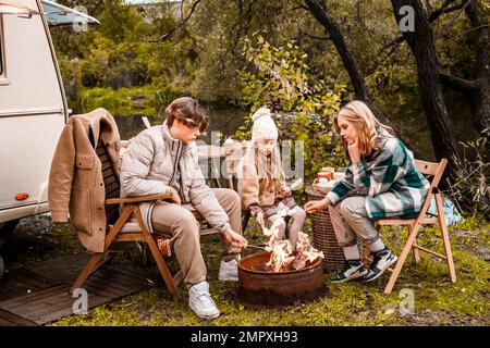 Bambini, famiglia, sorella fratello friggere marshmallows sul fuoco. Picnic nella natura. Sedia di legno, table.barbecue barbecue cibo. Viaggio di vacanza, fine settimana di vacanza dinne Foto Stock