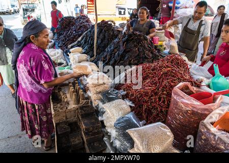 Una donna indigena Zapotec acquista una borsa di fagioli nel mercato di Ocootlan de Morelos a Oaxaca, Messico. Ha il suo reboso o scialle tradizionale avvolto Foto Stock