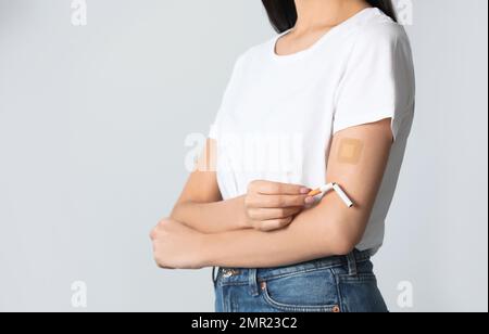 Giovane donna con nicotina cerotto e sigaretta su sfondo grigio chiaro, primo piano Foto Stock