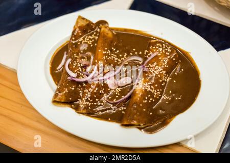 Enchiladas vegetariane preparate al momento con salsa al talpa servita in un ristorante locale a Puebla. Cucina messicana tradizionale a base di ingredienti freschi Foto Stock